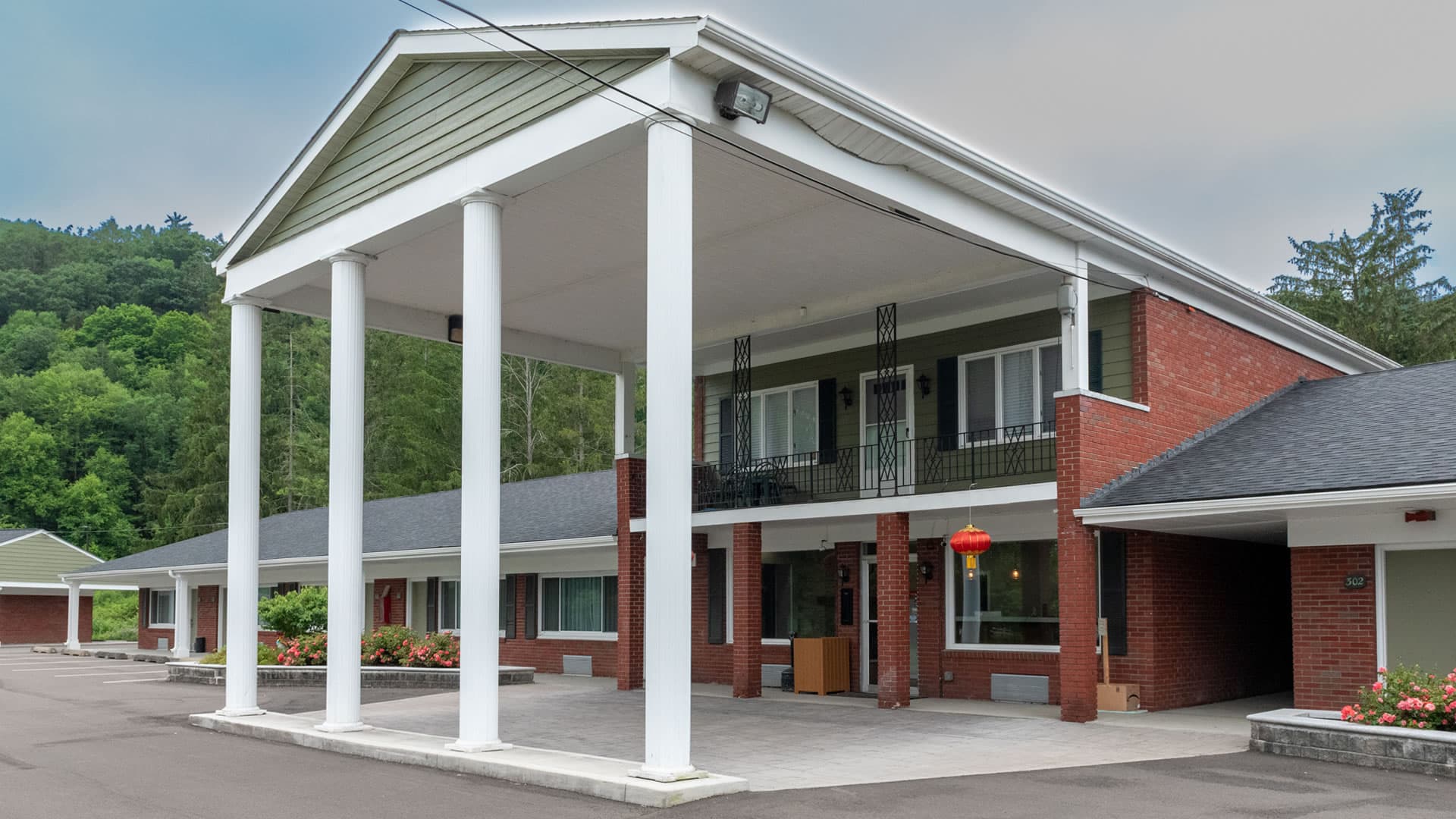 A brick motel with a large, columned entrance surrounded by greenery.